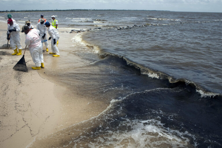 Workers clean up oil balls from Deepwater Horizon oil spill as the surf brings more onto a beach in Waveland